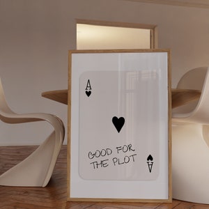 May include: A framed print of a playing card with a black heart and the text "Good for the plot" on a white background.
