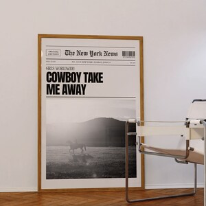 May include: A black and white photo of a person riding a horse in a field. The photo is framed and hanging on a white wall. The text "The New York News" is printed at the top of the photo. The text "GIRLS WORLDWIDE COWBOY TAKE ME AWAY" is printed below the photo.