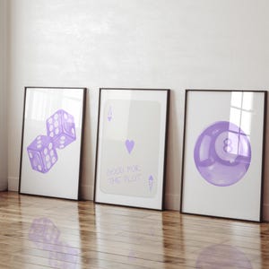 May include: Three framed prints with a white background and purple illustrations. The left print features two purple dice. The center print features a purple ace of spades playing card with the text "Good for the Plut." The right print features a purple eight ball.