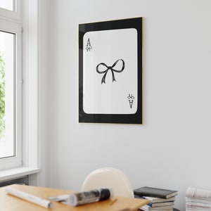May include: A black and white framed print of an ace of spades playing card with a black bow in the center.