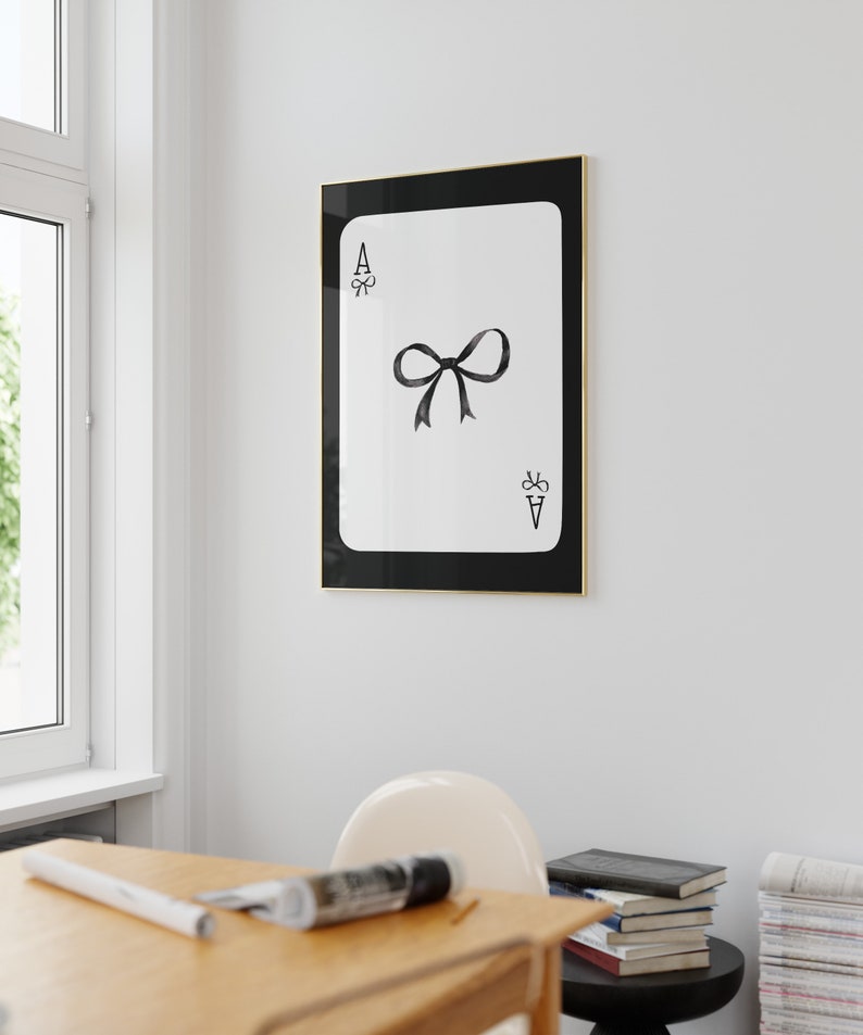 May include: A black and white framed print of an ace of spades playing card with a black bow in the center.