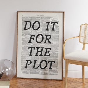 May include: Framed vintage newspaper print with the text "DO IT FOR THE PLOT" in bold black letters. The print is in a wooden frame and leans against a white wall. A chair with a gold frame and a glass sphere are in the image.