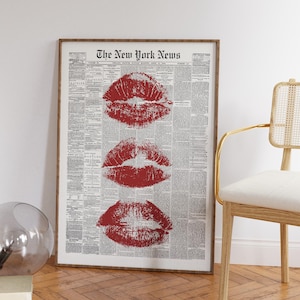 Può includere: Opera d'arte incorniciata con tre impronte di baci di rossetto rosso su uno sfondo di giornale d'epoca. Il giornale è intitolato "The New York News". L'opera d'arte è esposta in una stanza con una sedia e una sfera di vetro.