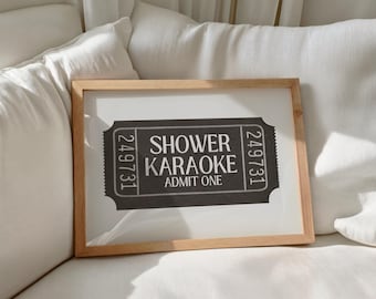 May include: A framed print with a light wood frame. The print features a black and white ticket design with the words "SHOWER KARAOKE ADMIT ONE". The ticket has the number 249731 on each side.