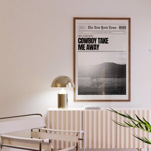 May include: A framed black and white newspaper print with the headline "COWBOY TAKE ME AWAY" and a photo of a horse and rider in a field. The newspaper is titled "The New York News" and has a special edition label.