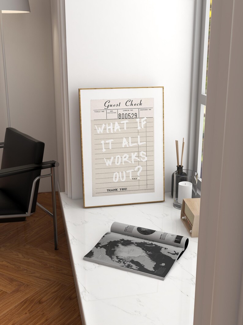 Puede incluir: Una impresi&oacute;n enmarcada de un "Guest Check" vintage con el texto "WHAT IF IT ALL WORKS OUT?" en blanco. Una revista enrollada con un mapa en blanco y negro est&aacute; frente al marco. Tambi&eacute;n se ven una vela, un difusor y una radio.