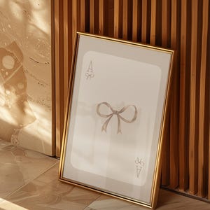 May include: A framed print of a playing card with a bow on it. The card is the Ace of Spades. The frame is gold.
