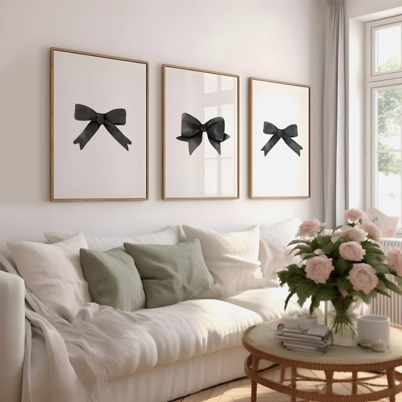 K&ouml;nnte beinhalten: Drei gerahmte Schwarzwei&szlig;-Aquarell-Illustrationen von Schleifen an einer wei&szlig;en Wand &uuml;ber einem wei&szlig;en Sofa mit gr&uuml;nen Kissen.