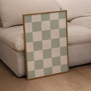 Puede incluir: Una impresi&oacute;n enmarcada con un patr&oacute;n a cuadros en tonos de verde y blanco. La impresi&oacute;n se apoya en un sof&aacute; blanco.