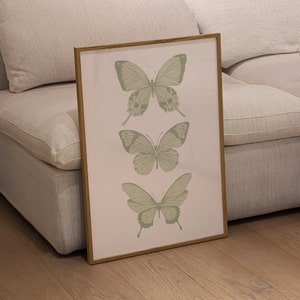 May include: A framed print featuring three green butterflies on a white background. The butterflies are arranged vertically, with the largest butterfly at the top and the smallest butterfly at the bottom.