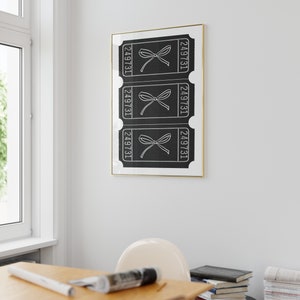 May include: Black and white print of three ticket stubs with the number 249731 on each. The tickets have a bow on them. The print is framed in gold and hanging on a white wall.