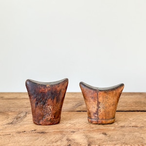 May include: Two antique wooden objects with a curved top and a flared base. The wood has a dark, aged appearance with variations in color, ranging from deep brown to lighter tan. They are displayed on a wooden surface.
