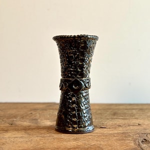 Puede incluir: Un jarrón de cerámica verde oscuro con una superficie texturizada y una banda decorativa alrededor del centro.