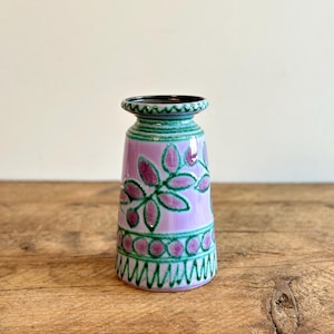 Puede incluir: Un pequeño jarrón de cerámica de color lila claro con un diseño floral verde y rosa. El jarrón tiene una base redondeada y una abertura ligeramente acampanada.