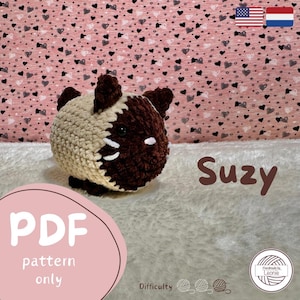 Puede incluir: Un juguete de amigurumi de gato tejido a crochet con pelaje marrón y beige. El juguete se llama "Suzy" y está disponible como patrón PDF. El patrón está hecho a mano por Lennie.