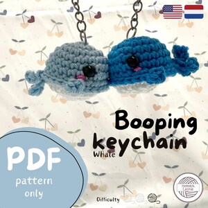 Puede incluir: Un patrón de crochet para un llavero de ballena. El patrón está disponible para descargar en PDF. El llavero presenta dos ballenas, una azul y otra azul claro, con ojos negros y mejillas rosadas. Las ballenas están tejidas a crochet en un estilo realista y están unidas a una cadena plateada. El patrón está etiquetado como "Llavero Booping Whale" e incluye una clasificación de dificultad.