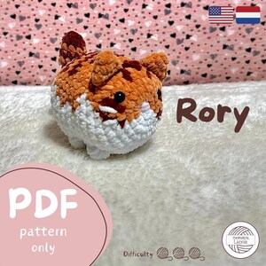 Puede incluir: Un juguete de peluche de crochet llamado Rory. El gato es naranja y blanco con ojos negros y una nariz rosa. El juguete está sentado sobre una superficie blanca y esponjosa. El texto "PDF pattern only" está escrito en rosa sobre un fondo blanco. El texto "Difficulty" está escrito en negro sobre un fondo blanco. Hay tres ovillos de lana al lado del texto "Difficulty". El texto "Handmade by Leonie" está escrito en negro sobre un fondo blanco con un icono de ovillo de lana. El texto "Rory" está escrito en marrón sobre un fondo blanco.