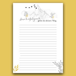 Könnte beinhalten: Ein liniertes Notizbuch mit einer Bergillustration und dem Text "Leise & erfolgreich gehst du deinen Weg." Das Design umfasst schwarze Vögel, goldene und graue botanische Akzente. Das Notizbuch hat einen weißen Hintergrund und einen gelben Rand.