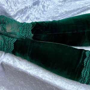 May include: A pair of dark green velvet gloves with lace trim. The gloves are fingerless with lace detailing on the hand and at the wrist. The velvet has a soft, luxurious appearance.