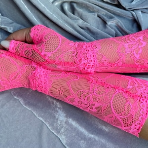 May include: A pair of pink lace fingerless gloves with a floral pattern. The gloves are made of a delicate, sheer fabric and extend to the elbow.