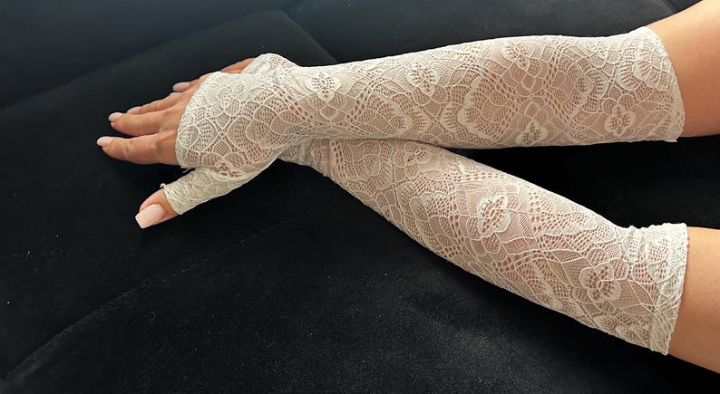 Puede incluir: Calentadores de brazo de encaje blanco roto con un patr&oacute;n floral. Los guantes sin dedos est&aacute;n hechos de una tela delicada y transparente. Los calentadores de brazo est&aacute;n dise&ntilde;ados para cubrir el antebrazo y se extienden hasta los nudillos.