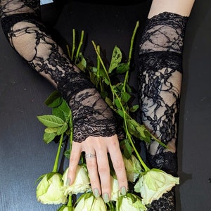 May include: A pair of black lace fingerless gloves with a bouquet of white roses. The roses have green stems and leaves.