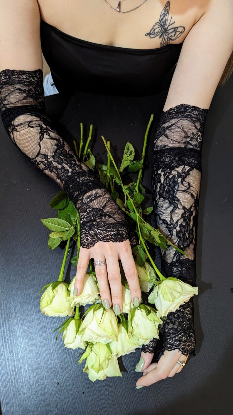 May include: A pair of black lace fingerless gloves with a bouquet of white roses. The roses have green stems and leaves.