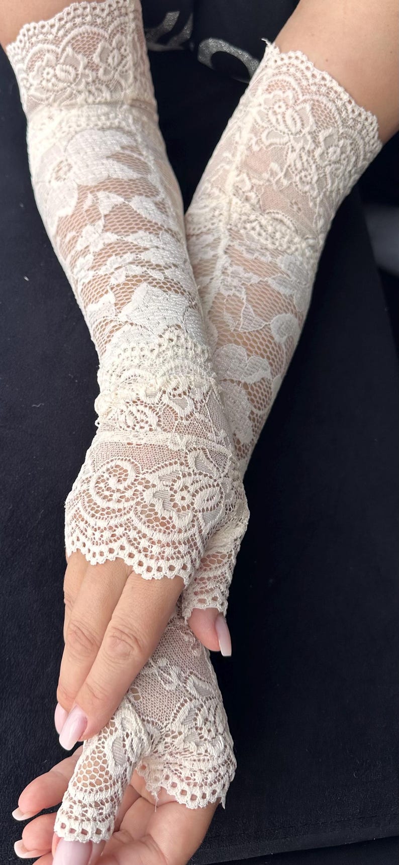 Op de afbeelding: Ivoor kanten vingerloze handschoenen. De handschoenen hebben een ingewikkeld bloemenpatroon en zijn gemaakt van delicate, transparante kant. De handschoenen zijn ontworpen om de hand tot aan de pols te bedekken, met een open ontwerp voor de vingers.
