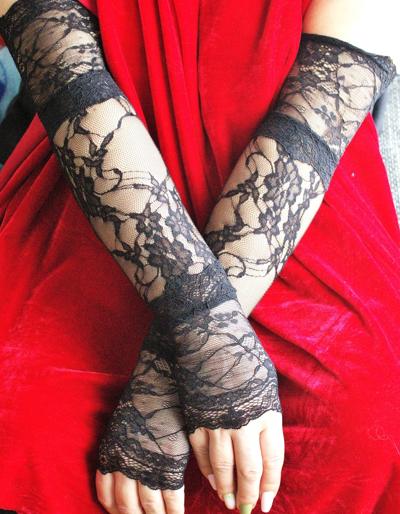 May include: A pair of black lace fingerless gloves with a floral pattern. The gloves are worn on both arms and are crossed over each other.