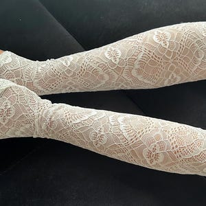 Puede incluir: Un par de mangas de encaje blanco. Las mangas est&aacute;n hechas de un delicado encaje con estampado floral. Las mangas se extienden desde la mu&ntilde;eca hasta la parte superior del brazo, con un dise&ntilde;o sin dedos. El fondo es de color oscuro s&oacute;lido.