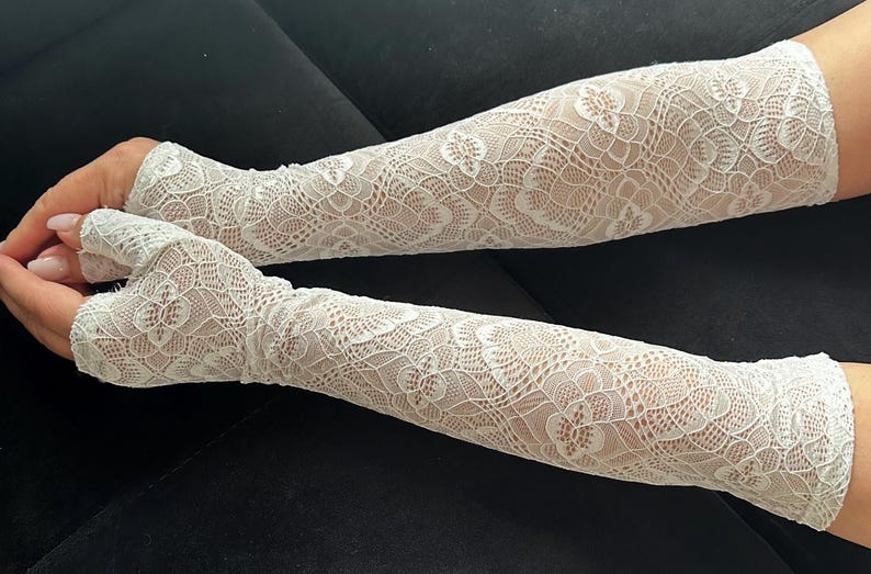 Puede incluir: Un par de mangas de encaje blanco. Las mangas est&aacute;n hechas de un delicado encaje con estampado floral. Las mangas se extienden desde la mu&ntilde;eca hasta la parte superior del brazo, con un dise&ntilde;o sin dedos. El fondo es de color oscuro s&oacute;lido.