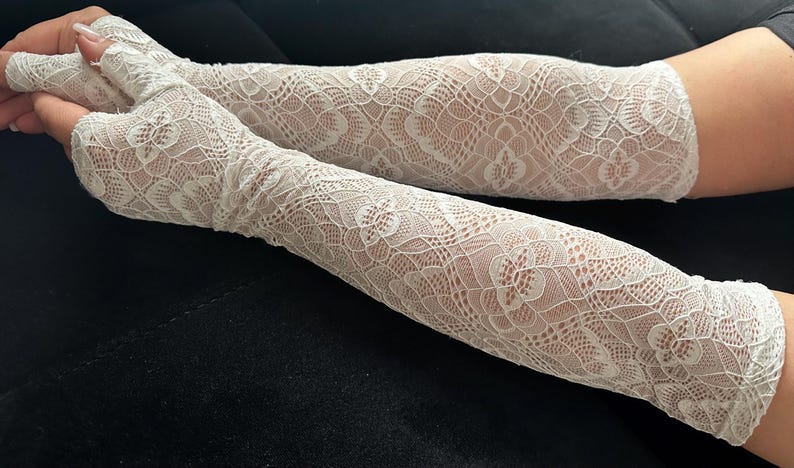 Puede incluir: Un par de calentadores de brazo de encaje blanco. Los guantes sin dedos se extienden por el brazo, con un delicado dise&ntilde;o floral. Los pu&ntilde;os est&aacute;n acabados con un borde festoneado. La tela es semitransparente.