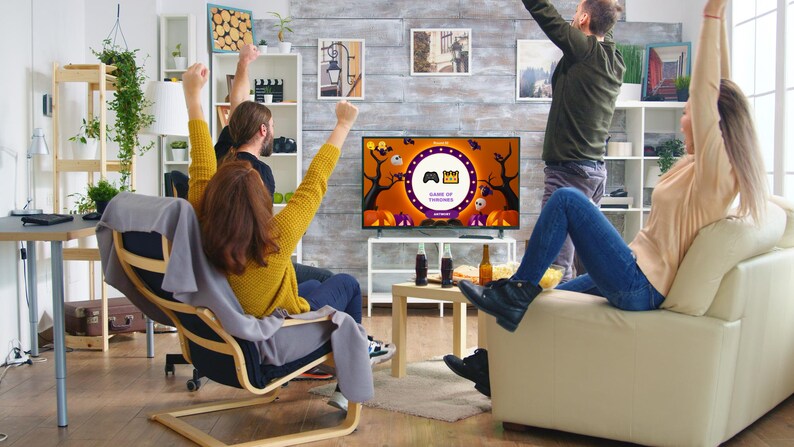 May include: Four friends are gathered around a television watching a Halloween-themed game show called "Game of Thrones". The television screen is decorated with pumpkins, bats, and a spooky forest. The friends are all smiling and cheering.