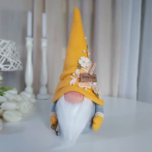 May include: A yellow gnome with a white beard and a yellow hat decorated with white flowers and a tag that says "Happy Easter".