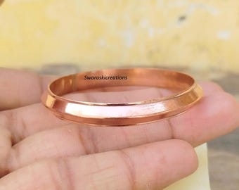 May include: A copper bangle with a smooth, rounded surface and a slightly raised edge. The bangle is shown on a hand, with the text "Swaroskikcreations" visible on the inside of the bangle.