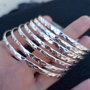 Puede incluir: Un conjunto de pulseras de plata martilladas. Las pulseras están apiladas una encima de la otra y tienen una superficie texturizada.