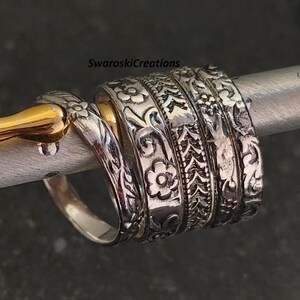 May include: Five silver rings with intricate floral designs stacked on top of each other. The rings are on a silver surface.