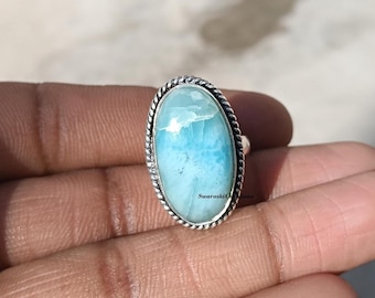 May include: Oval-shaped ring featuring a light blue gemstone with white marbling, set in a silver-toned metal band with a twisted rope design around the stone. The ring is displayed on a hand.