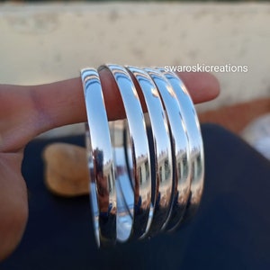 Peut inclure: Cinq bracelets argentés empilés, montrant la surface lisse et brillante du métal.