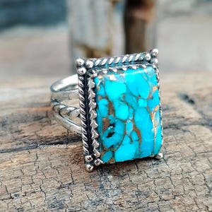 May include: A silver ring with a turquoise stone set in a square bezel. The stone has a marbled pattern of blue and gold.