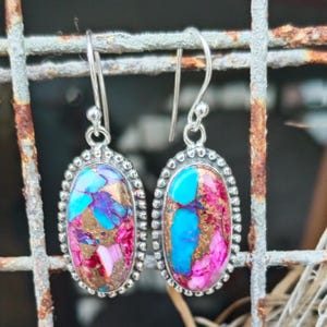 Puede incluir: Un par de pendientes colgantes de plata con piedras ovaladas de color turquesa, rosa y oro. Las piedras tienen un patrón de mármol.