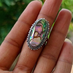 May include: A silver ring with an oval abalone shell inlay. The shell has iridescent colors of pink, green, and blue.