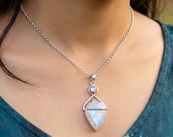 May include: A silver chain necklace featuring a teardrop-shaped moonstone pendant topped with a smaller round moonstone. The metal setting has a polished finish. The text Swaroskicreations is visible on the surface of the larger stone.