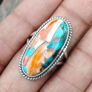 May include: Oval shaped ring with a silver band and a large turquoise, coral, and white stone inlay.