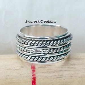 May include: A silver spinning ring with a braided design. The ring has five bands with a textured finish.
