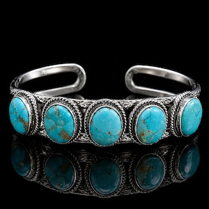 Può includere: Un bracciale a fascia in argento con cinque pietre turchesi di forma ovale con motivi a matrice marrone. La fascia metallica presenta un bordo a corda intrecciata attorno a ogni pietra e un intricato motivo inciso lungo i lati.