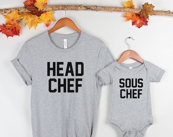 Könnte beinhalten: Ein graues T-Shirt mit dem Text "HEAD CHEF" in schwarzen Buchstaben. Daneben ein grauer Baby-Strampler mit dem Text "SOUS CHEF" in schwarzen Buchstaben.