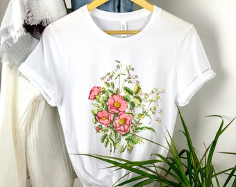 May include: White t-shirt with a floral print featuring pink flowers and green leaves.