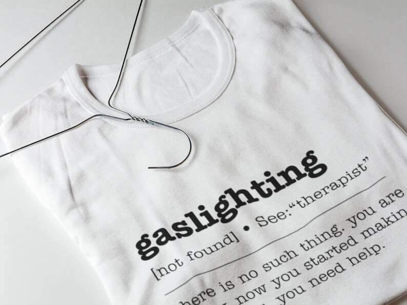 以下が含まれることがあります： 「ガスライティング」という言葉が定義された白いTシャツ。「[見つかりません]。参照：「セラピスト」そんなものはありません。あなたは今、作り始めています。助けが必要です。 」
