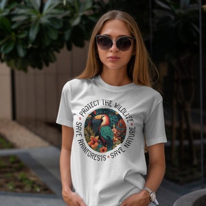 May include: White t-shirt with a colorful graphic of a toucan in a rainforest setting. The graphic is surrounded by the text "Protect the Wildlife Save Rainforests Save Nature".